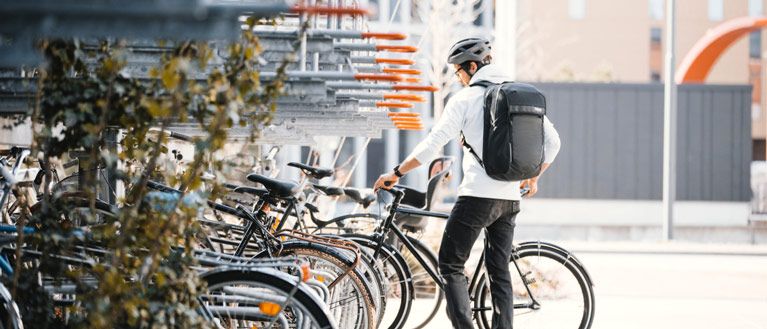 A man parks his bike by a train station wearing a Thule Paramount backpack.