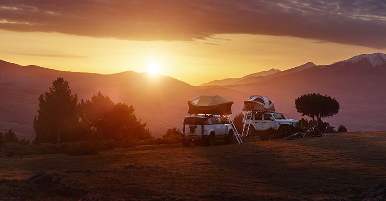The sun rises over mountains where two jeeps are parked with car roof tents.