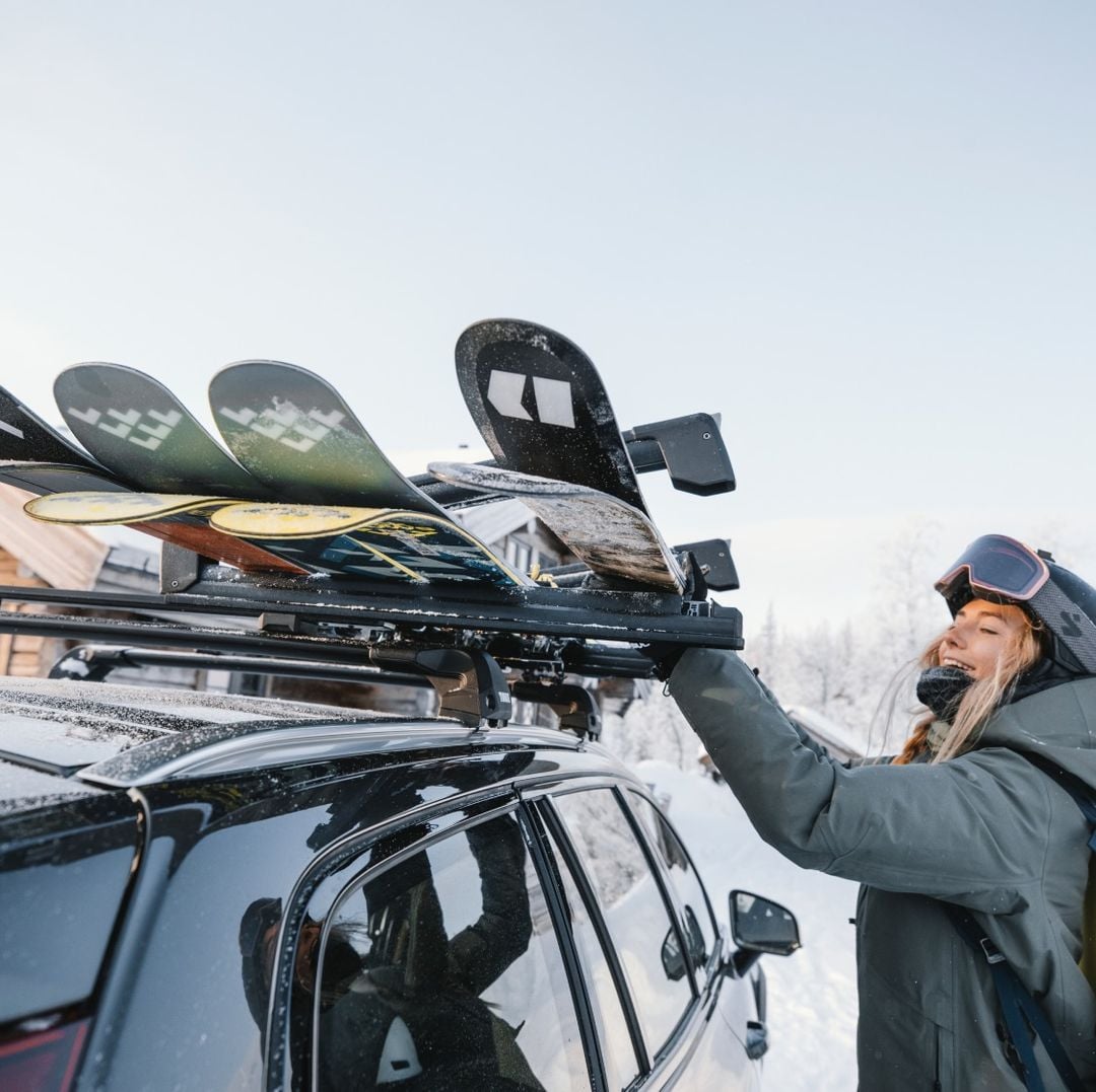 A woman removes skis from a Thule ski rack mounted to the roof of a car in the snow. 