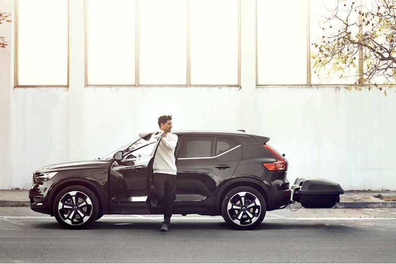 Un hombre sale de un automóvil negro que está estacionado en un estacionamiento con un baúl de carga trasero Thule Arcos.