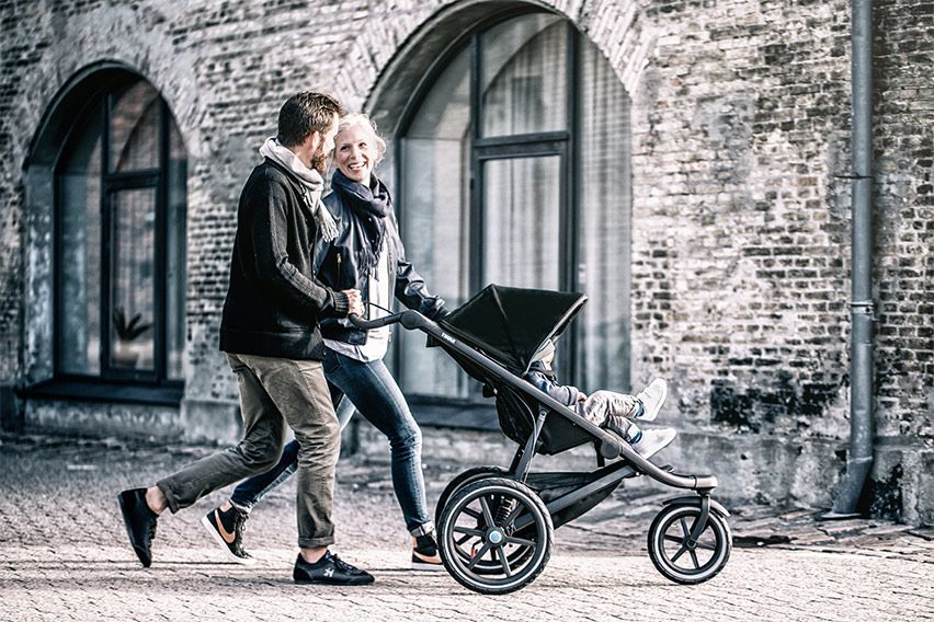 A woman and a man push their Thule baby carriage down a cobbled city street.