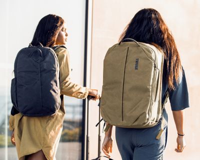 Two women walk down a street in the sunshine carrying travel backpacks.