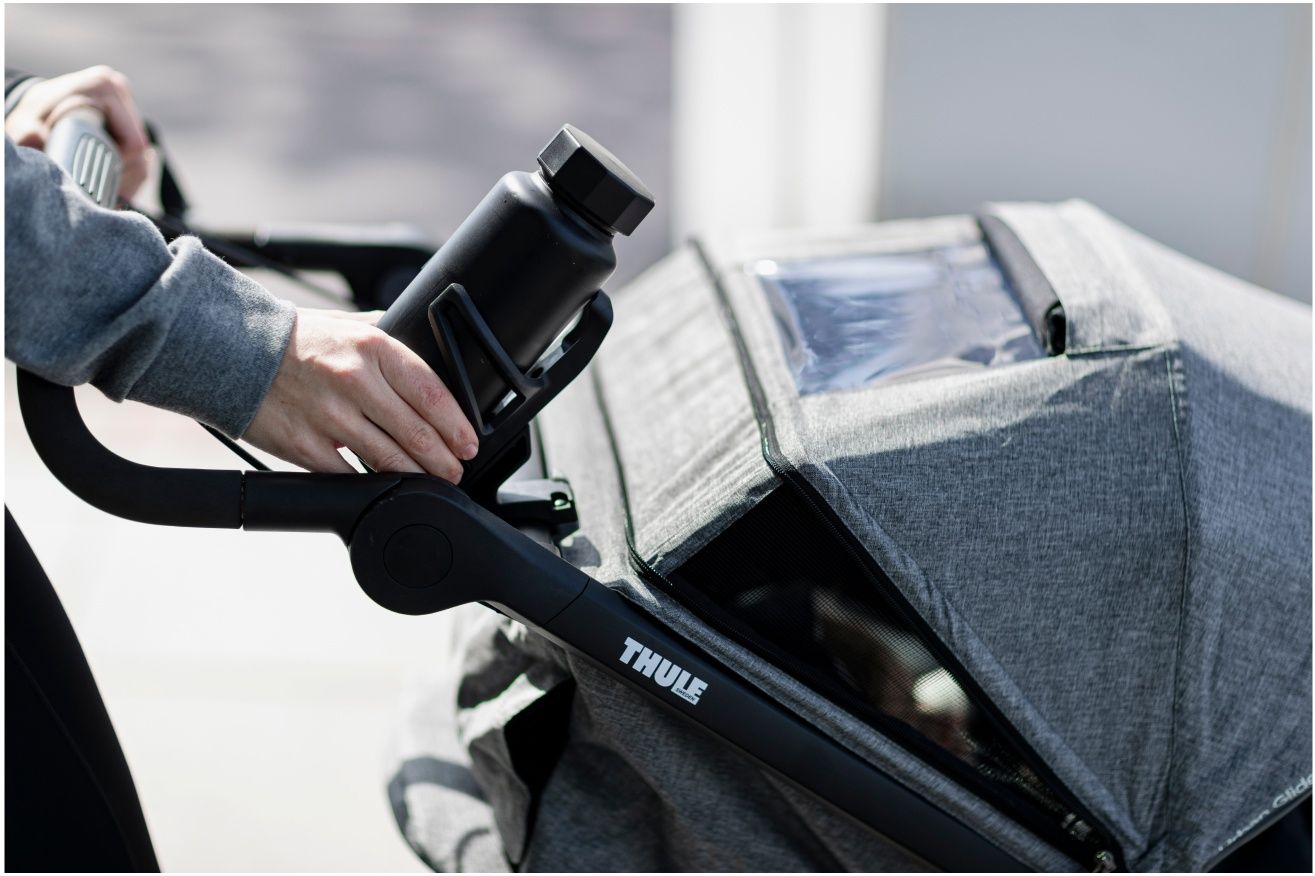 A close up of a woman putting her water bottle into the water bottle holder of a Thule jogging stroller.