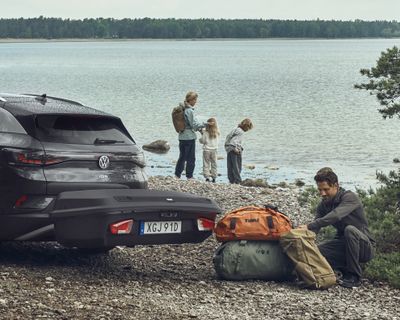 A vehicle is parked with a hitch cargo carrier on the beach and a family stand beside it.