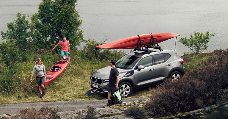 Two people carry their kayak ashore while a man stands beside his car with a kayak on the Thule kayak rack