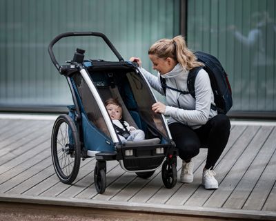Женщина смотрит на своего ребенка в велоприцепе с аксессуарами.