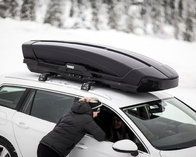 Una mujer habla con alguien dentro de un automóvil con un baúl de techo.