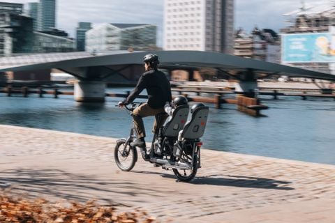 Een man rijdt op een longtail-fiets met twee kinderen die achterin kinderstoeltjes zitten. 