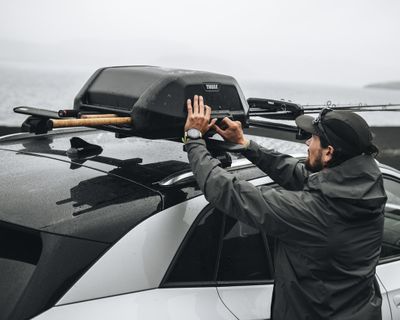 Un hombre descarga sus cañas de pescar de un vehículo con portacañas de pescar.