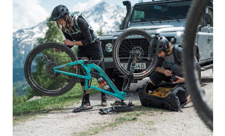 Two cyclists fix their bike with tools in a Thule RoundTrip bike gear bag.