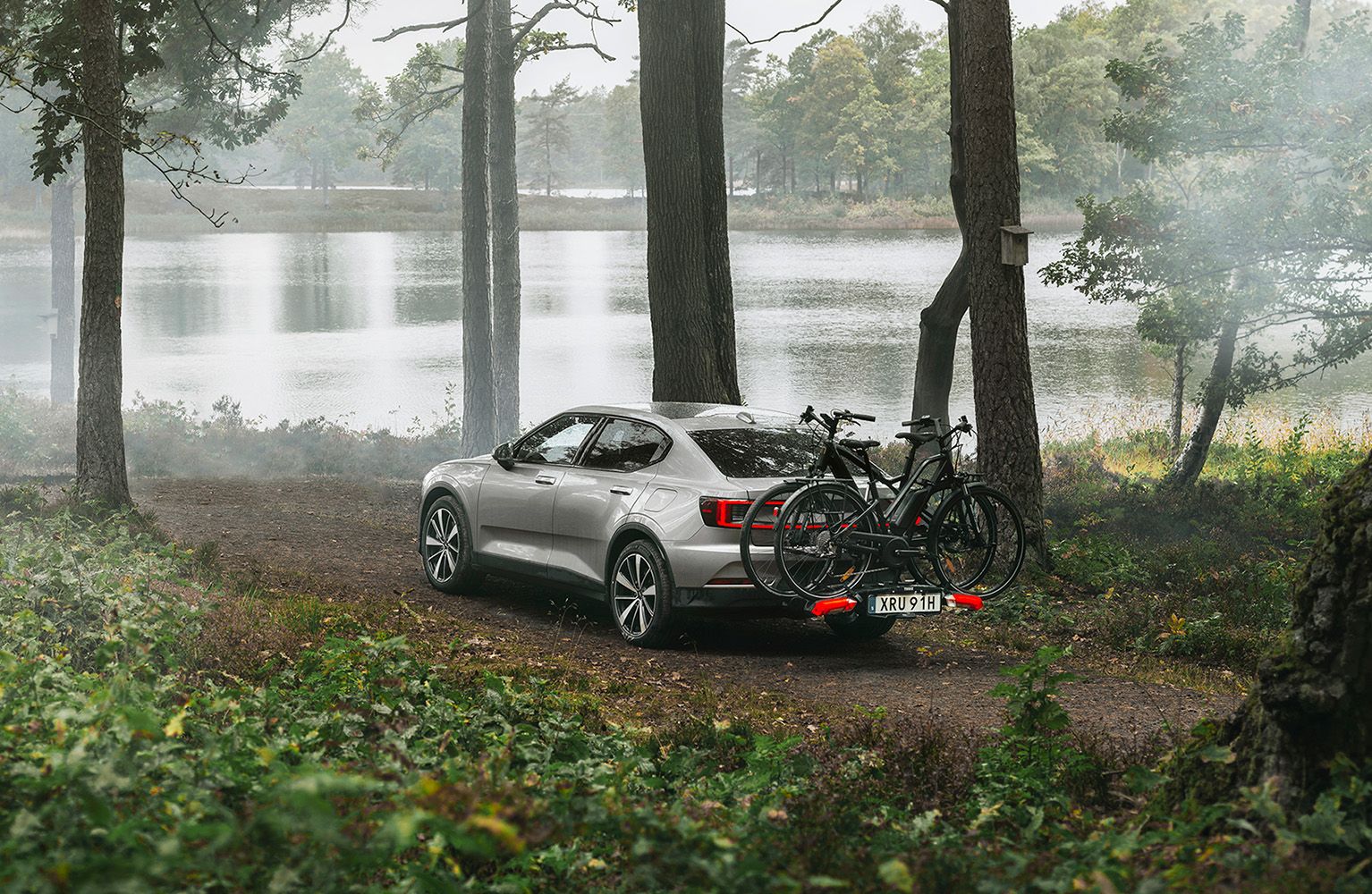 A car is parked in a forest by a lake with a Thule Epos bike rack.