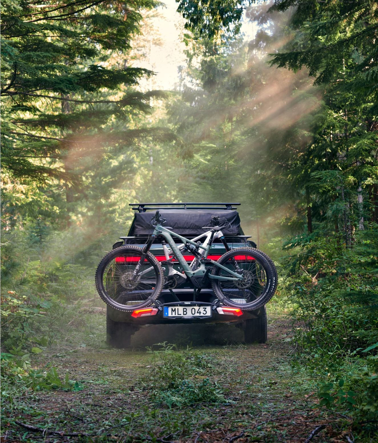 Texto ALT: Una camioneta estacionada al aire libre con dos bicicletas MTB cargadas en un portabicicletas Thule Epos.