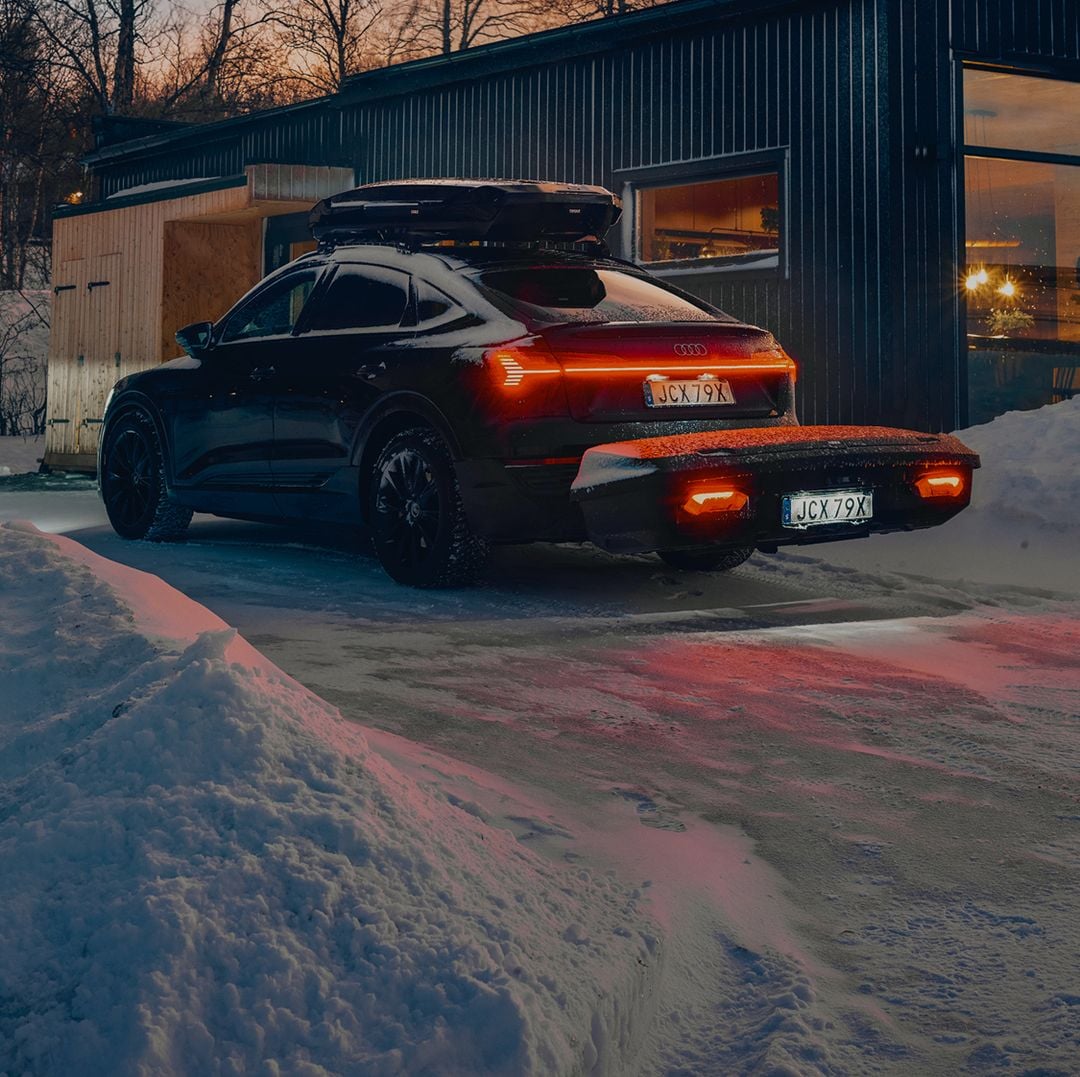 Car with Thule cargo carrier parked outside a snowy cabin at night.