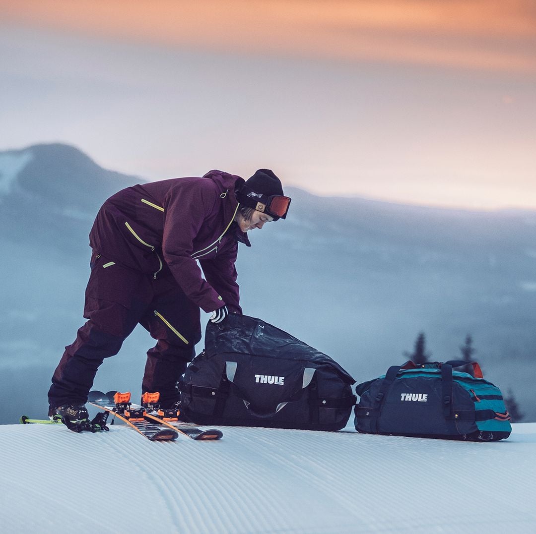 Person in Skiausrüstung, die Thule-Taschen auf einer verschneiten Piste packt.