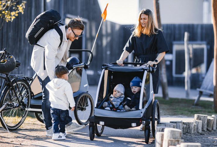 A woman strolls with two children in the Thule Courier bike trailer for kids.