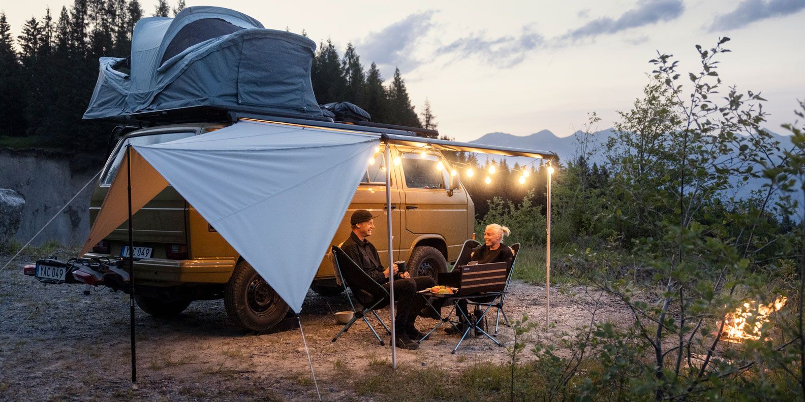A man and woman sit in camping chairs at night under their Thule Subsola awning panels.