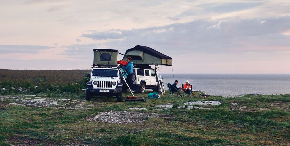 To personer sykler vekk fra et taktelt med mykt skall som står parkert i de snødekte fjellene.