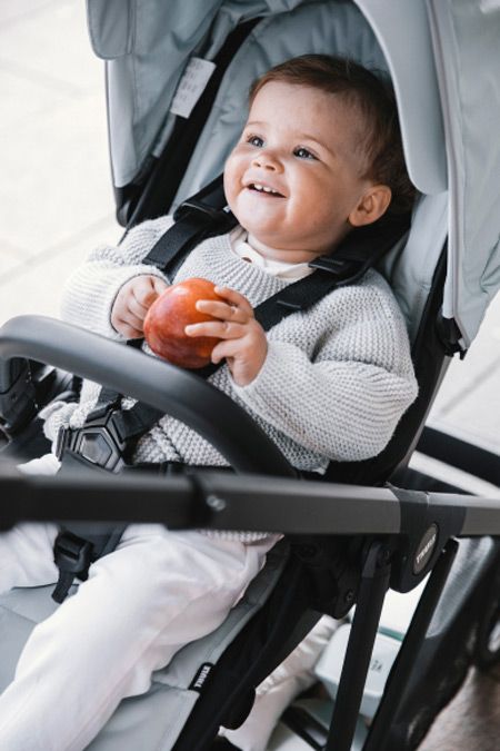 A close up of a child holding an apple in a Thule Shine stroller.