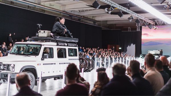 Two women sit on top of an SUV loaded with Thule gear while going down the runway at a fashion show.