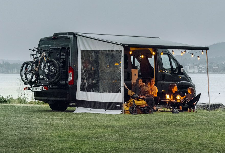 A motorhome is parked with an awning tent and a Thule VeloTrack bike rack.