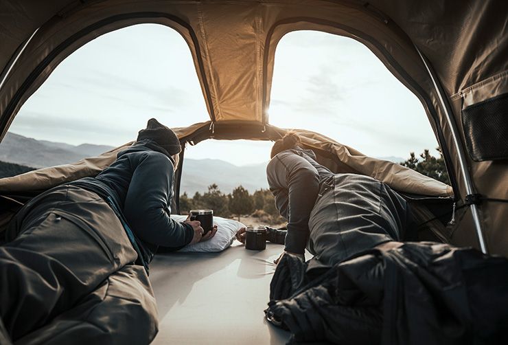 A couple sits in a Thule Approach car top tent looking out of the panoramic windows