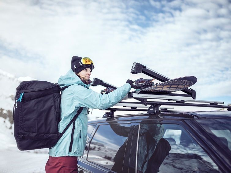 A woman loads snowboard into on of the Thule snowboard racks.