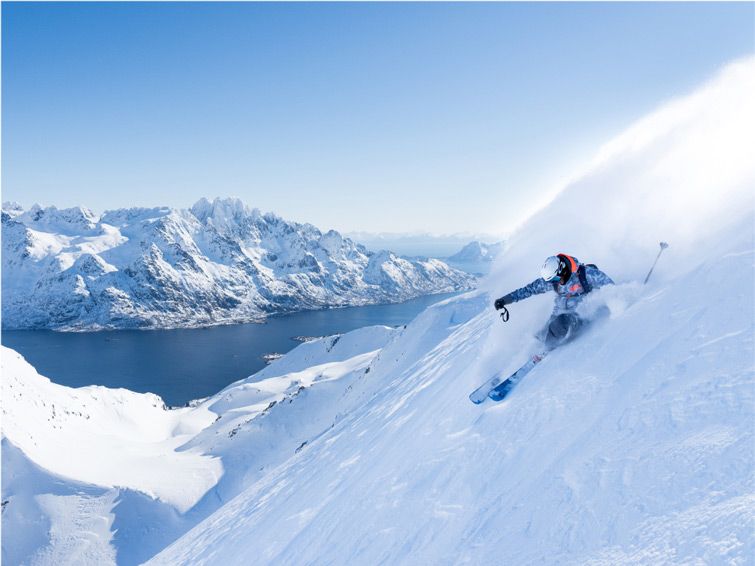 Lorenzo Alesi skis down a mountain at Lofoten in Norway, behind him mountains rise out of the water.