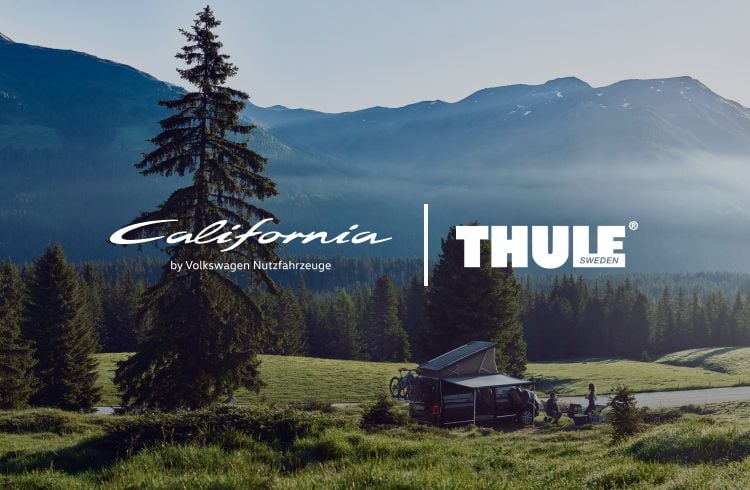 Ein Volkswagen California Campervan, ausgestattet mit Thule Campingausrüstung, in einer malerischen Berglandschaft, umgeben von Bäumen unter einem blauen Himmel.