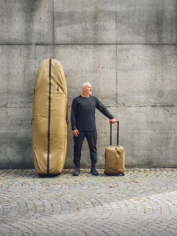 Garrett McNamara stojící vedle vaku na surfové prkno Thule Aion na pozadí městské betonové architektury.
