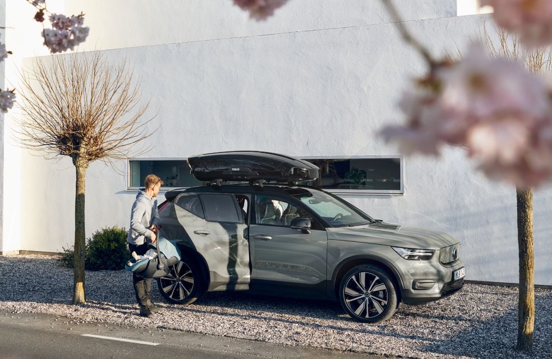 白い家の隣に停車した車の横に立つ男性が、Thule Maple乳児用チャイルドシートを後部座席に積み込もうとしています。