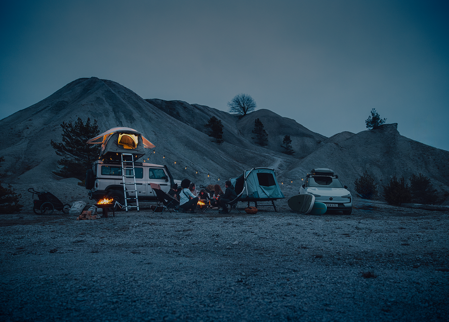 Mensen zitten in de schemering rond een kampvuur naast twee voertuigen die zijn uitgerust met Thule-tenten en -producten.