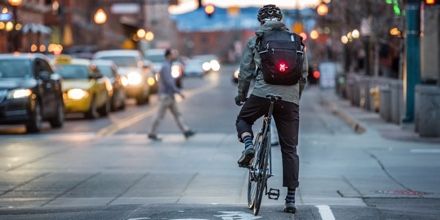 A man bikes in traffic at night with a cycling backpack with a red bike light on it.