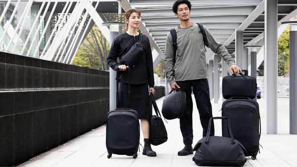 An Asian woman and man standing in an urban environment carrying and holding a collection of black Thule Subterra bags and suitcases.