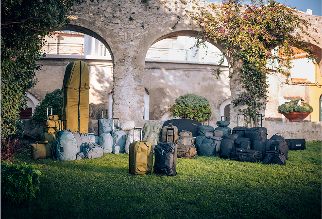 Alle Taschen von Thule sind für ein Gruppenfoto in einem grünen Garten aufgestellt.
