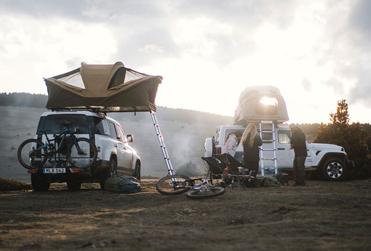 Два автомобиля с палатками Thule Approach на крышах и с велосипедами на велокреплениях припаркованы на траве