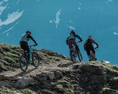 Drie fietsers met Thule Vital drinkrugzakken fietsen over een bergpad.