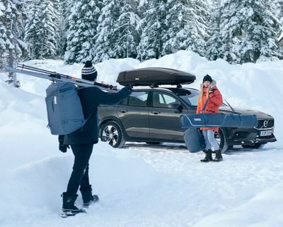 Nella neve, una donna con delle borse da sci saluta un uomo con una borsa da sci.