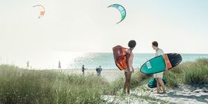 Two people stand with Thule backpack and a surfboard, looking out at the ocean. 