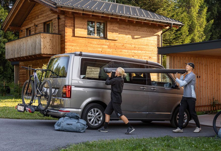 A man and a woman load the Thule Sidehill awning onto the removable adapters on their vehicle.