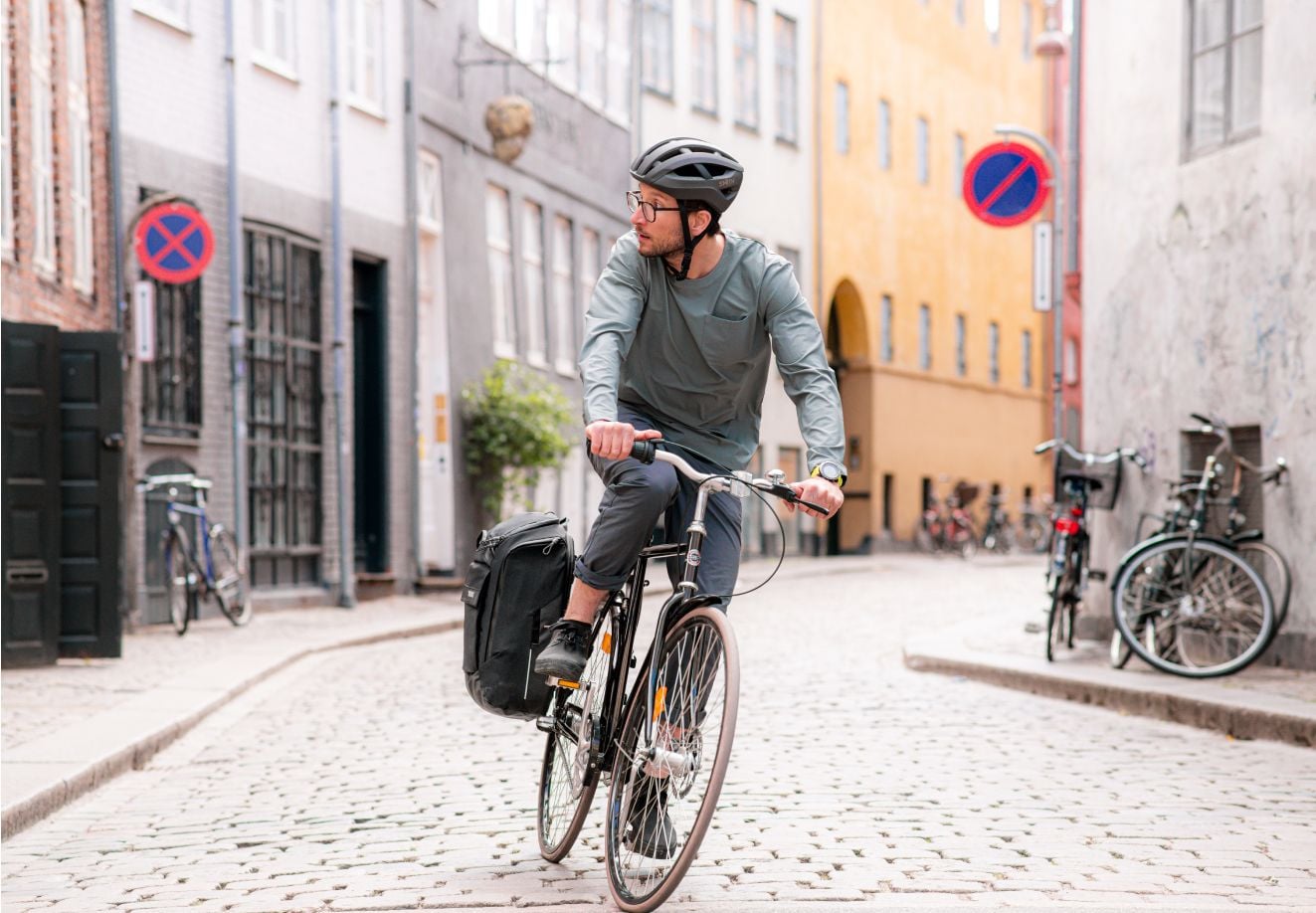 En person sykler i en by med en Thule Paramount-hybridveske festet til sykkelstativet.