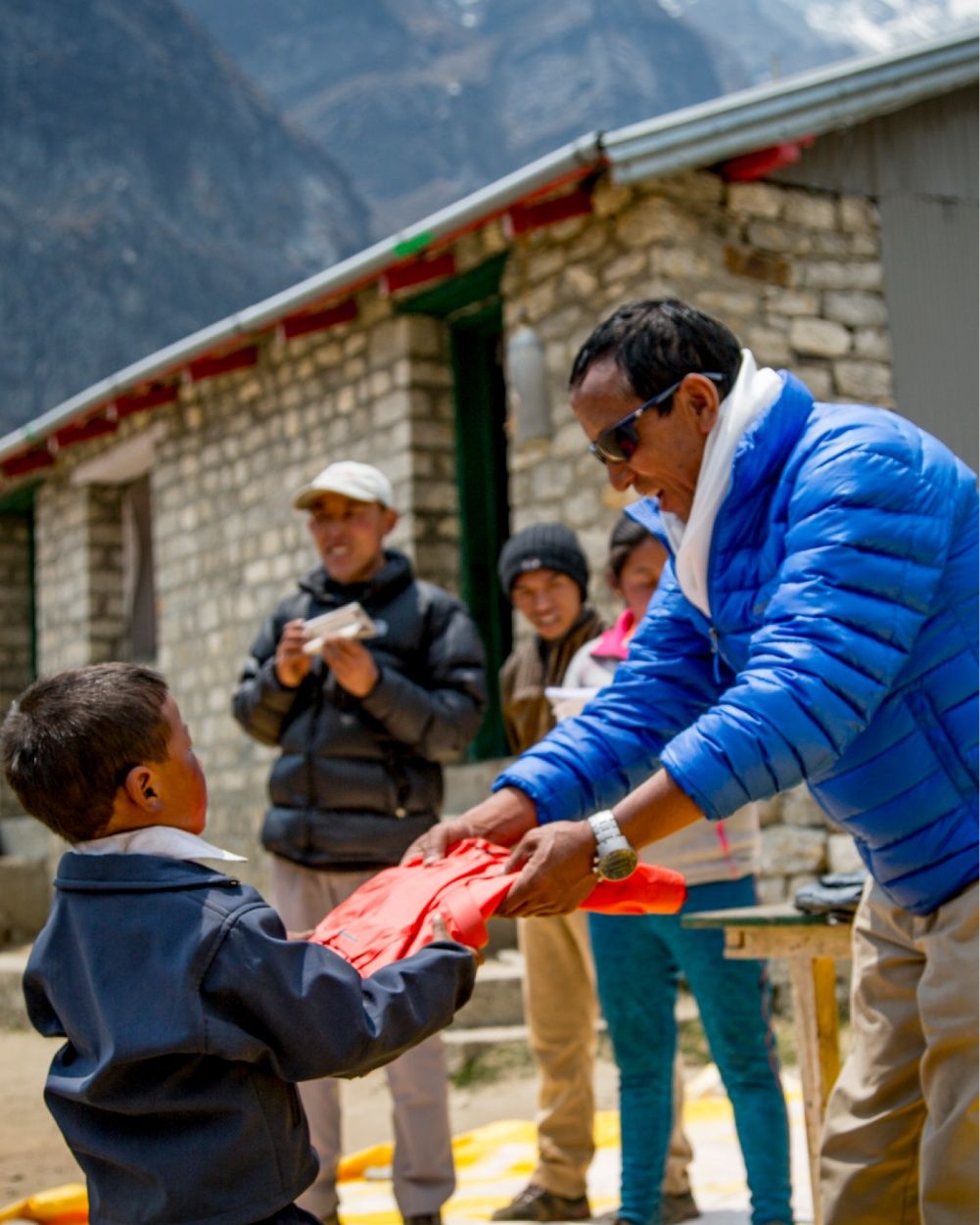 Apa Sherpa hands a red backpack to a child in a village.
