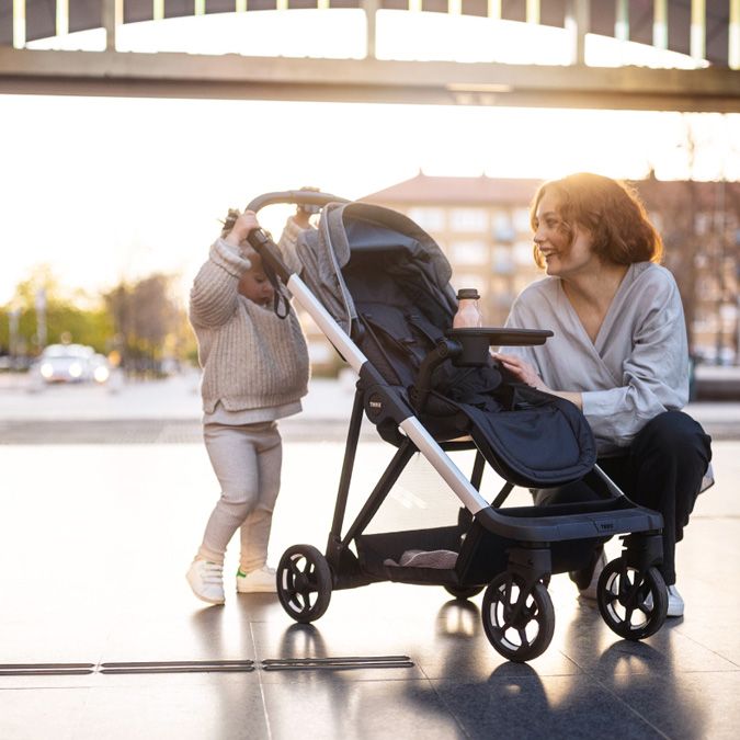 A toddler tries pushing her Thule Shine stroller while her mother watches.