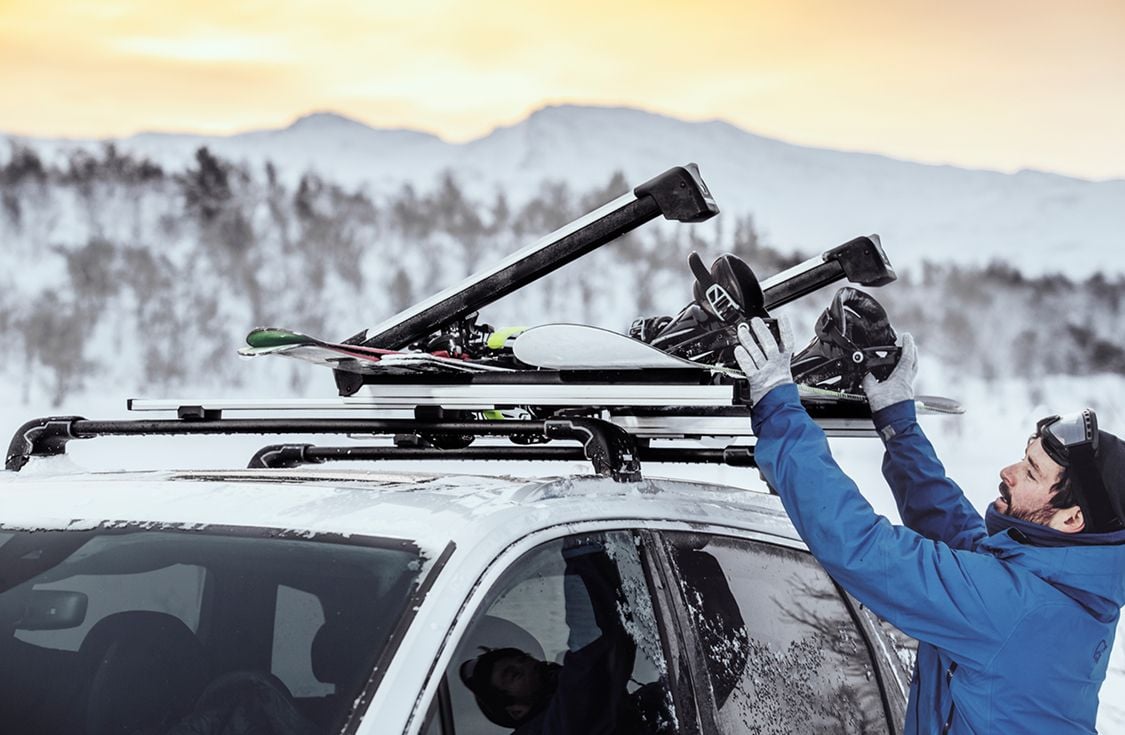Thule Outlet hero banner showing a skier loading gear onto a roof rack in a snowy mountain landscape.
