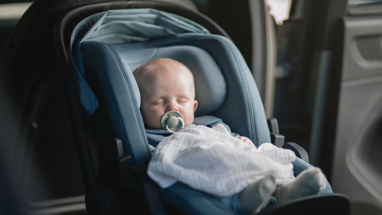 Un bambino addormentato in un seggiolino rivolto contro il senso di marcia, allacciato in modo sicuro con un ciuccio in bocca.