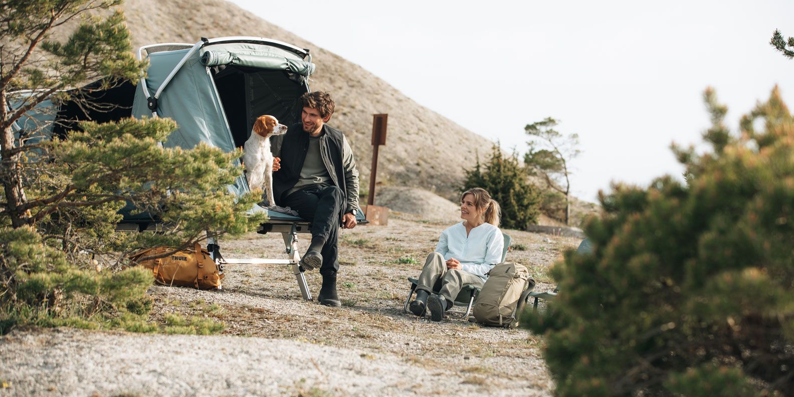 A man and a woman sit with their dog inside the Thule Outset car tent.