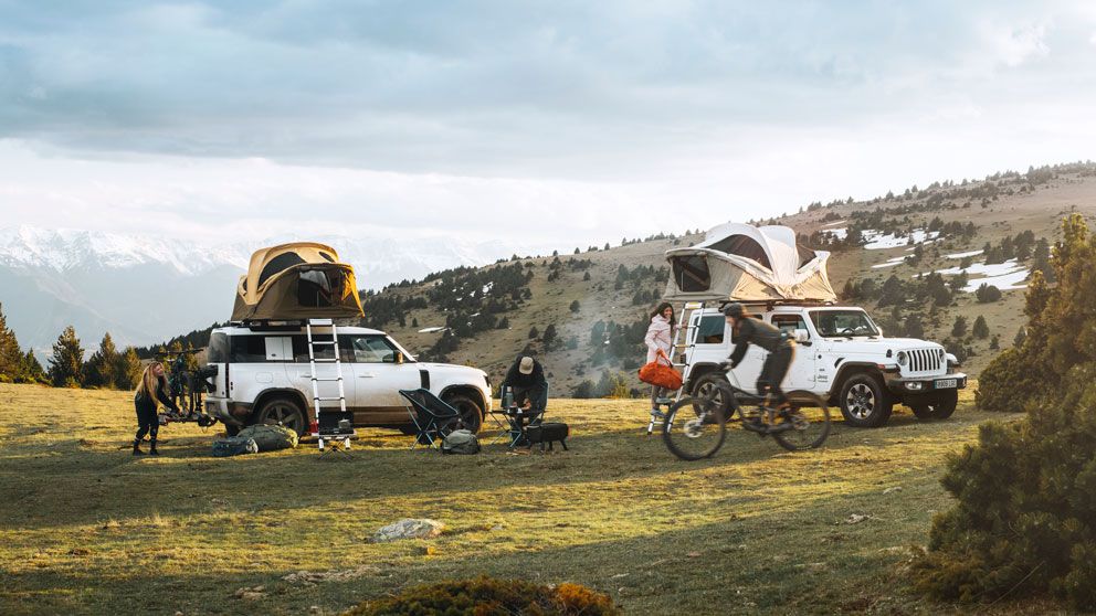 Two vehicles are parked in the snowy mountain with Thule Approach car top tents and people biking around.