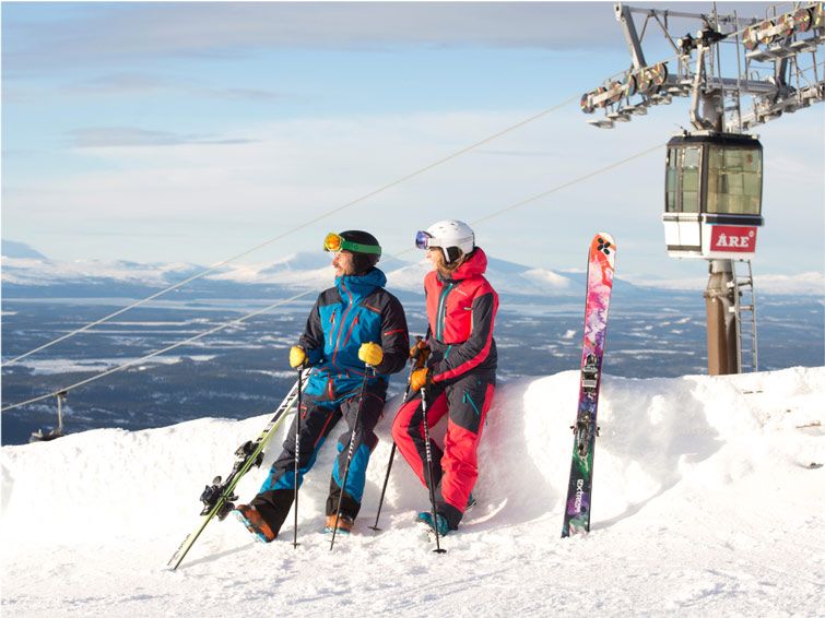 Two skiers sit with their ski gear and look over the expansive landscape below at Are ski resort in Sweden.
