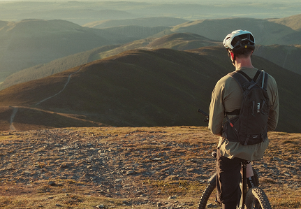 Um homem com uma mochila de hidratação Thule senta-se numa bicicleta enquanto observa as montanhas. 