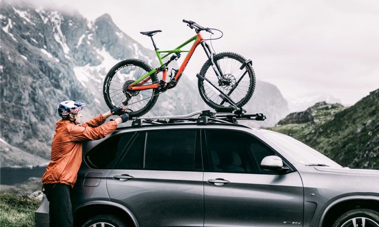 A man in the mountains unloads his bike from a Thule wheel mount roof bike rack.