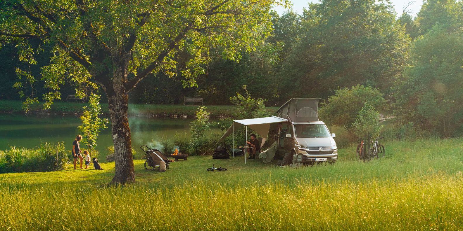 A vehicle is parked in a field next to a lake with the Thule Subsola awning panels.